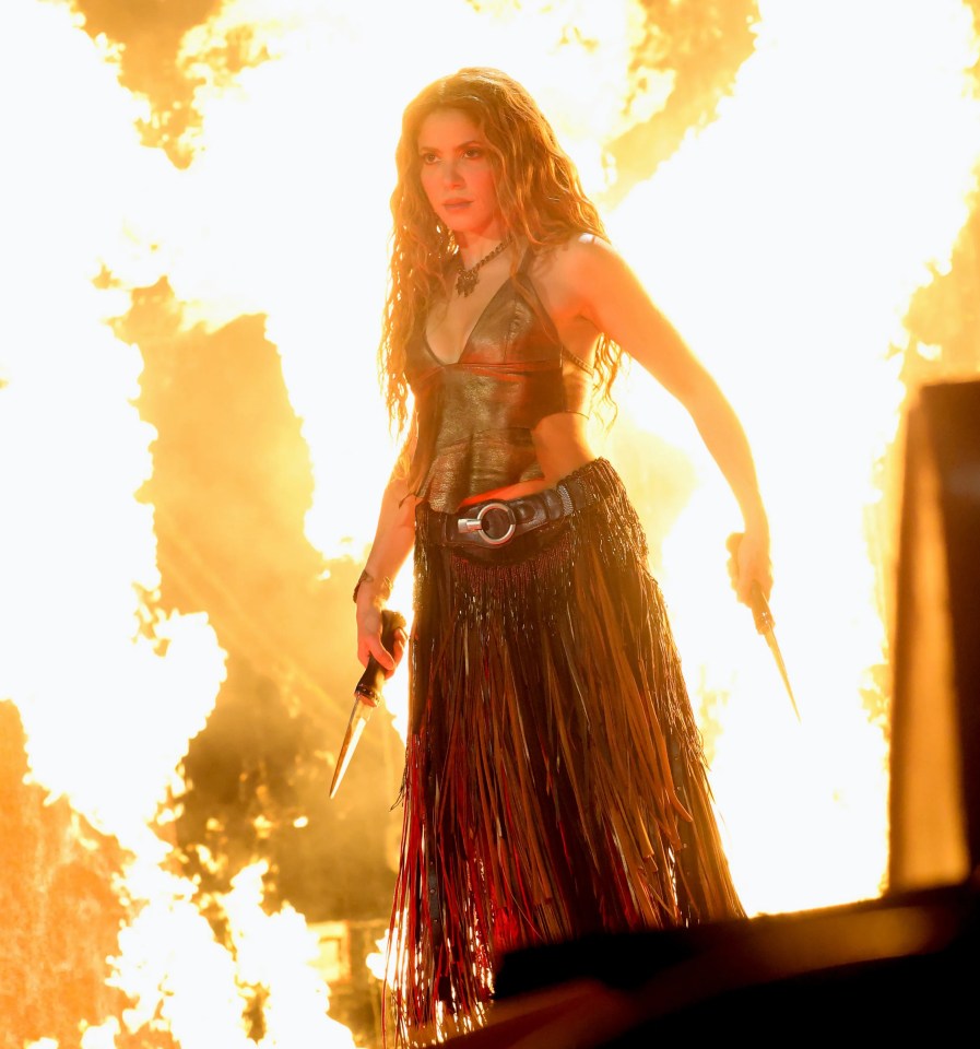 Shakira performing onstage with fire in the background.
