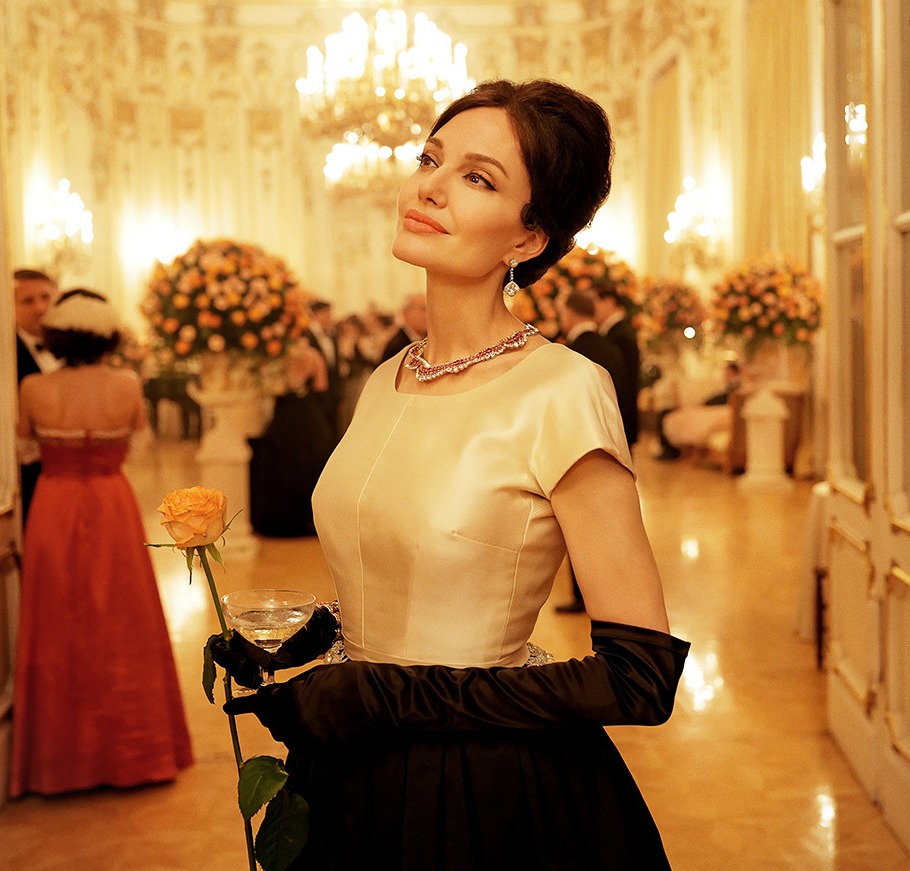 Angelina Jolie at a gala, holding a rose and a glass of champagne.