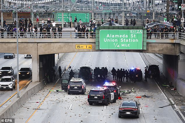 Police officers take cover as activists shower rocks and debris onto their vehicles during protests sparked by immigration raids in LA Sunday