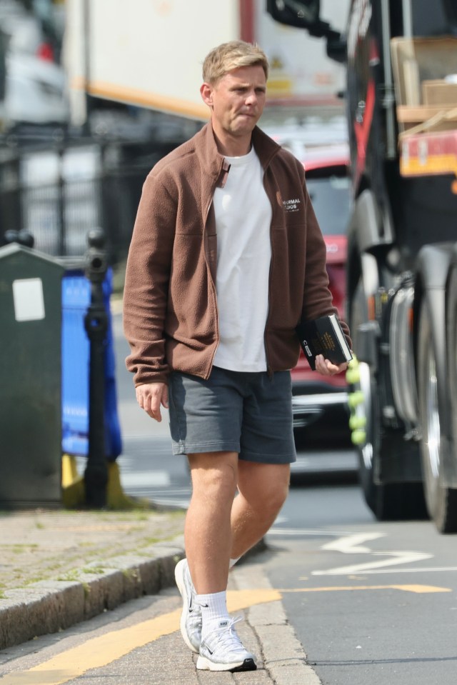 Jeff Brazier walking down a street, carrying a book.