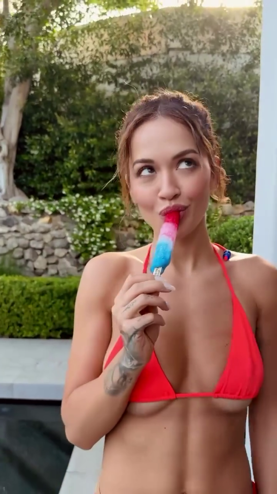 Rita Ora in a red bikini eating a popsicle.