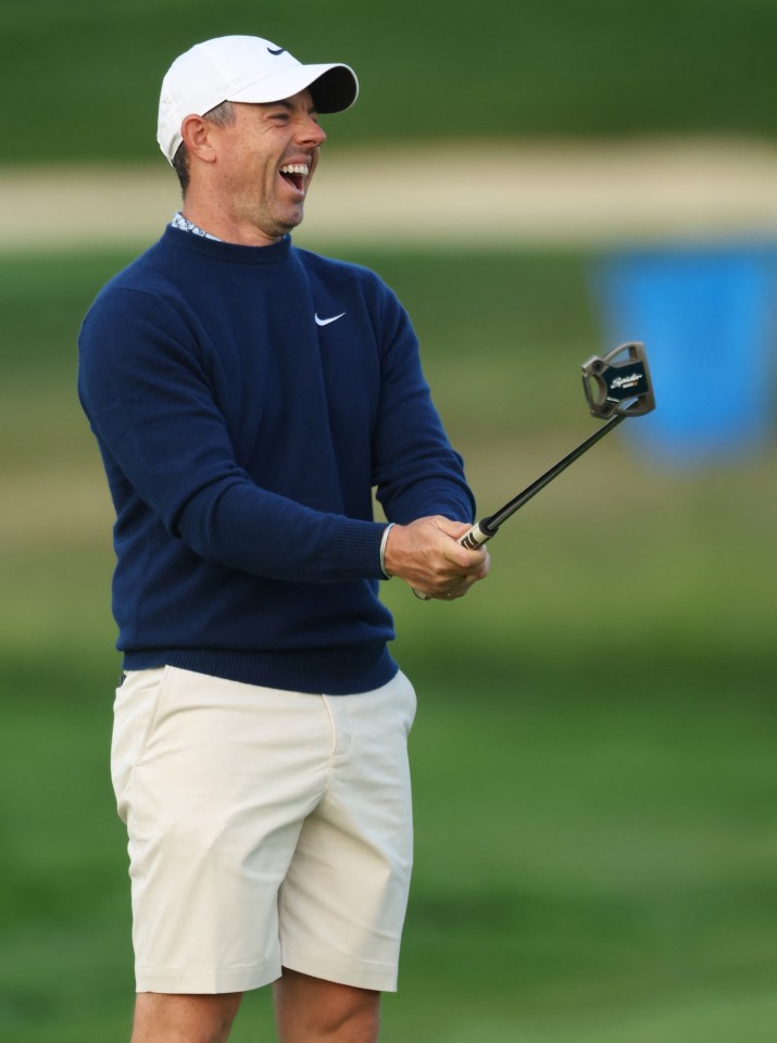 Rory McIlroy laughing while holding a golf putter.