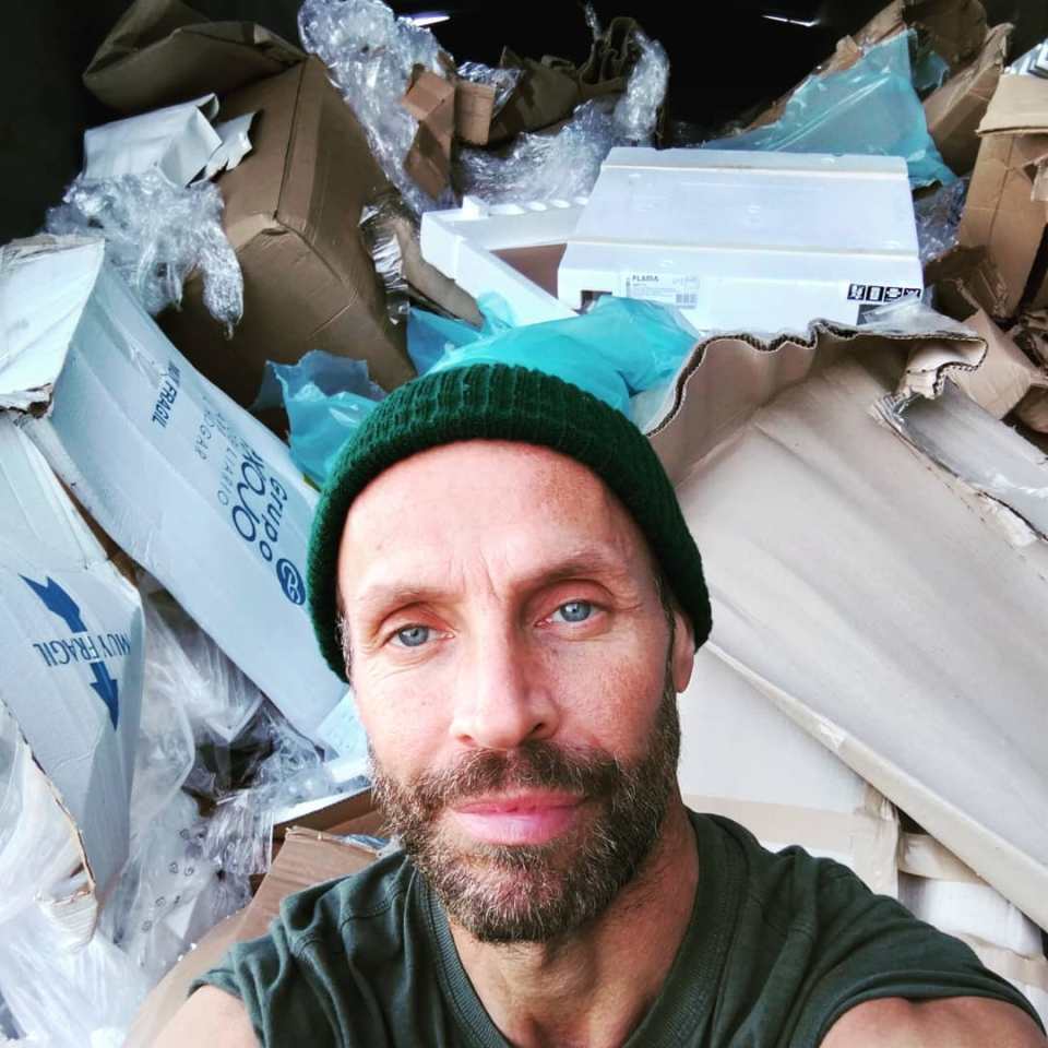 Selfie of a man with a beard and beanie amidst a pile of cardboard boxes and packing materials.