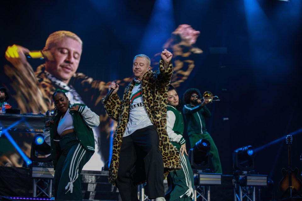 Macklemore performing on stage with backup dancers and musicians.