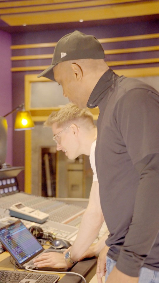 Two men working together on a laptop in a recording studio.