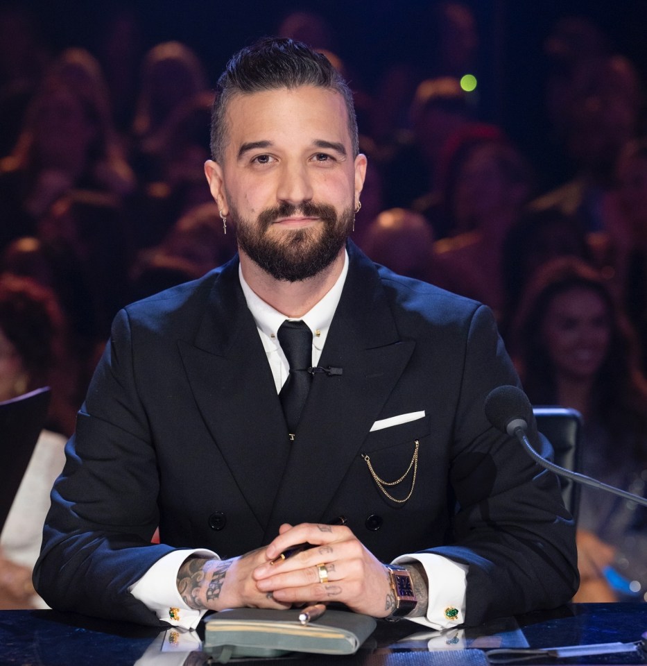 Mark Ballas sitting at a table in a suit.