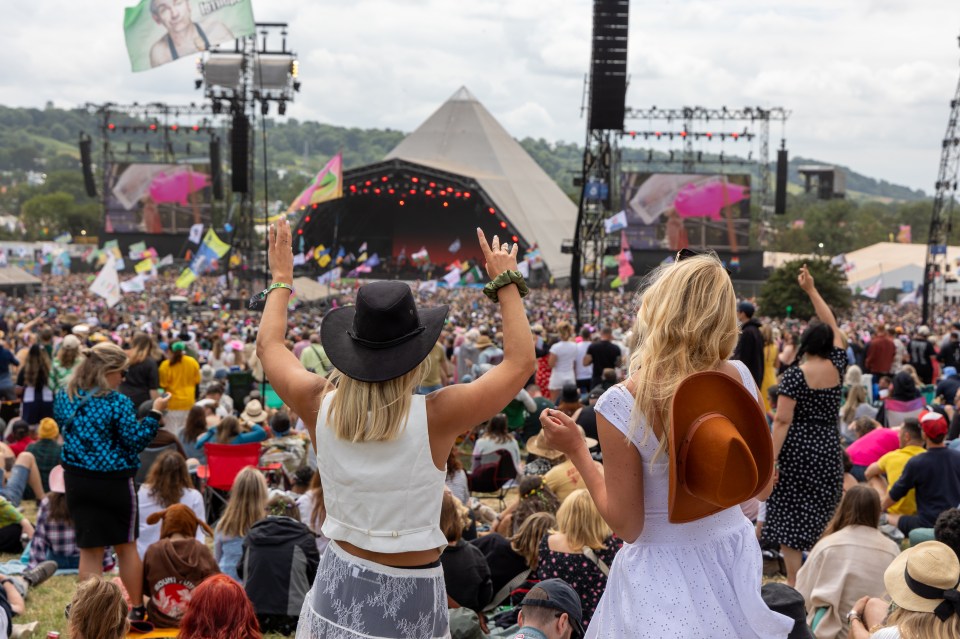 Crowd at Glastonbury Festival, viewed from behind two women with their arms raised.
