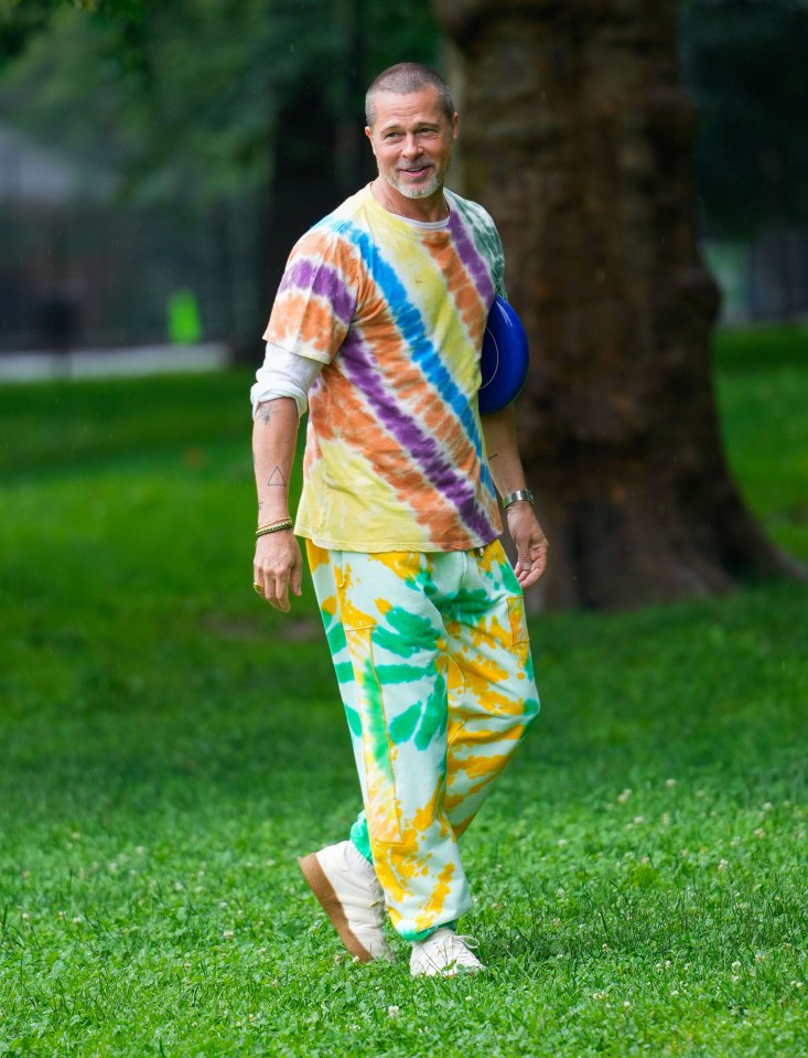 Brad Pitt in tie-dye shirt and pants walking in a park.