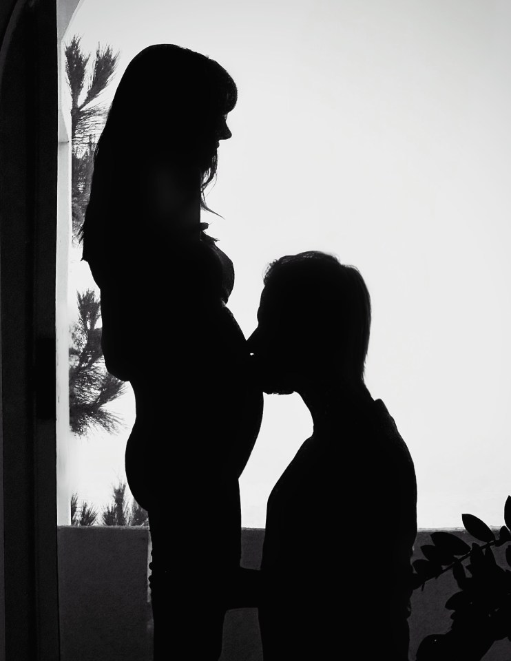 Silhouette of a pregnant woman being kissed on her belly by a man.
