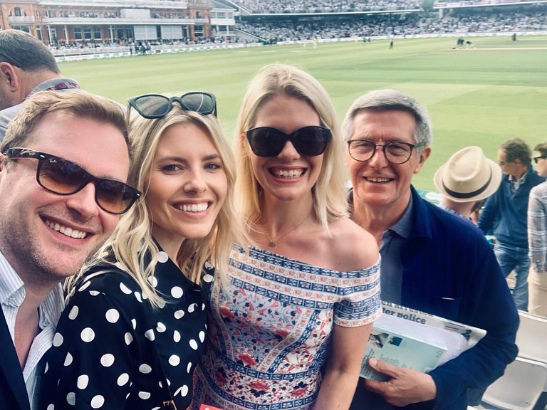 Group photo of four people at a cricket match.