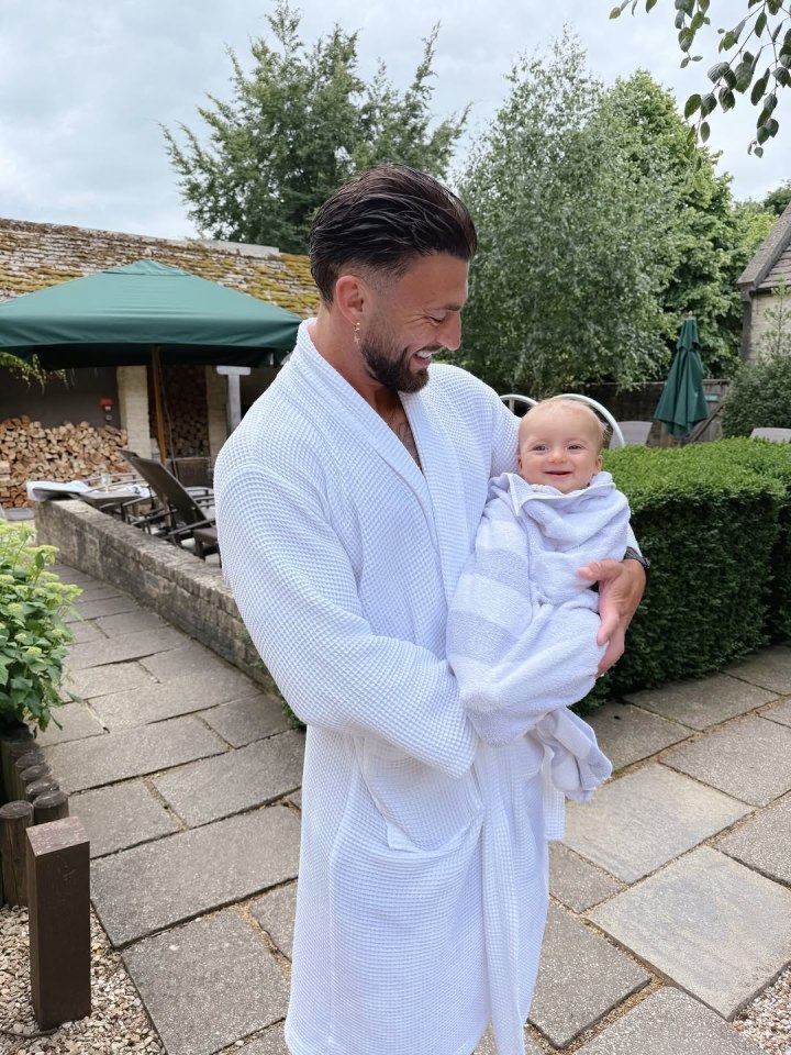 A man in a white robe holding a baby wrapped in a towel.