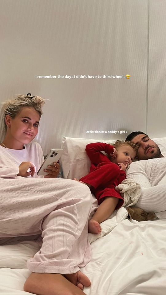 Woman on phone in bed with man and baby.