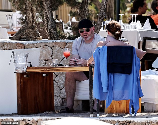 Wayne dressed casually in a light grey T-shirt and dark shorts