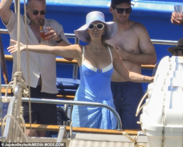 She accessorised with oversized white sunglasses and a wide-brimmed sunhat, flashing a huge smile as she laughed with friends and waved to onlookers