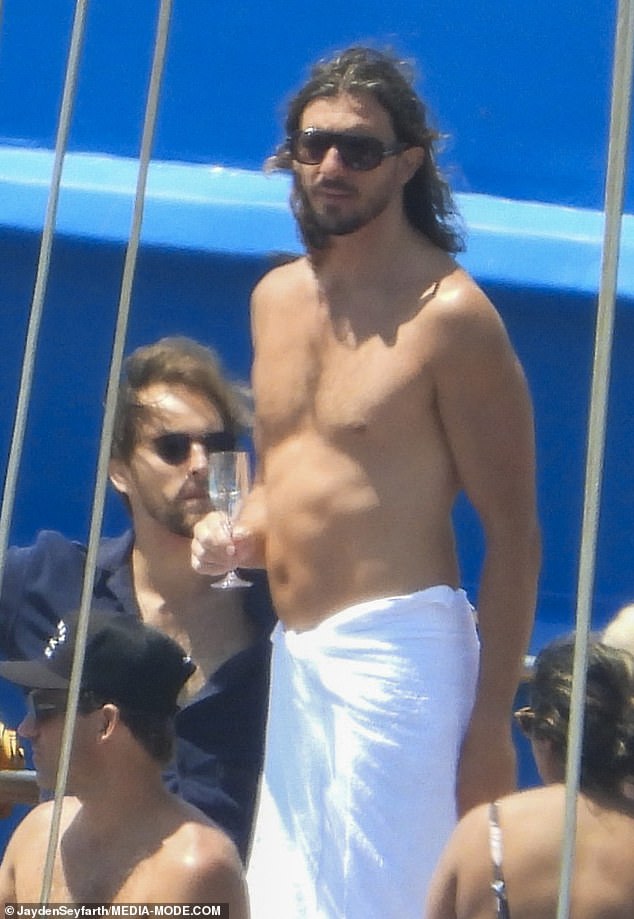 Later, he ditched the shirt and was seen relaxing on deck wrapped in a white towel, sipping champagne and chatting with friends