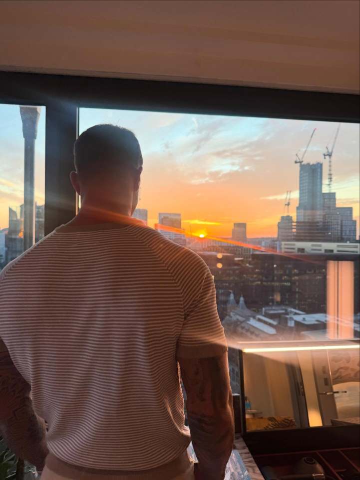 Person looking out window at sunset over city skyline.