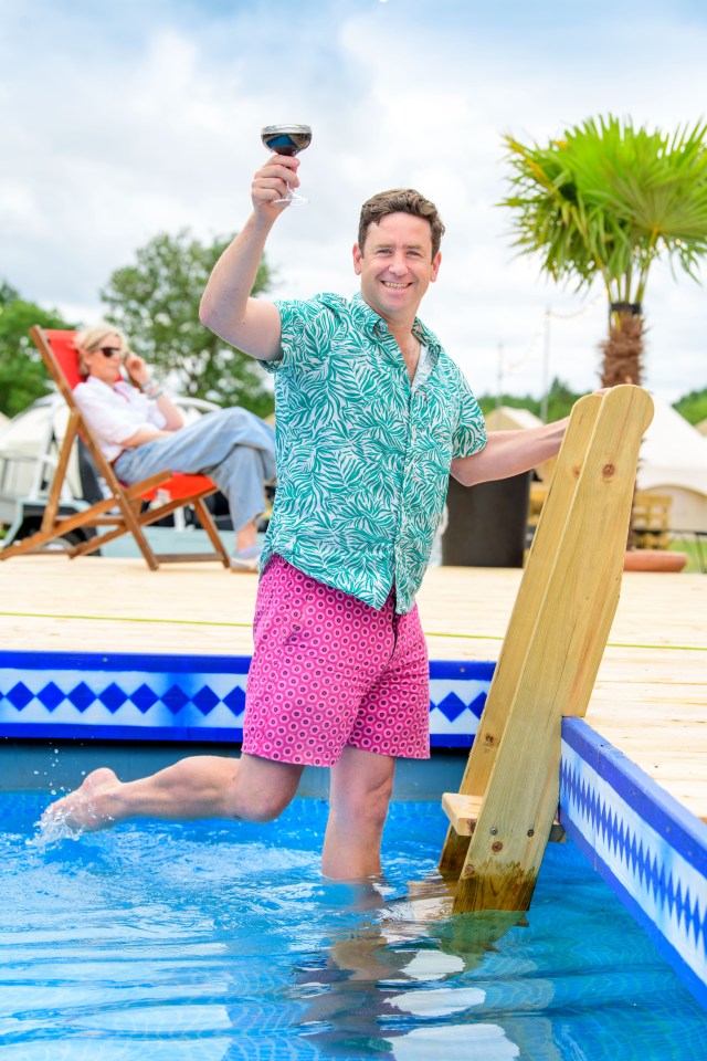 Man entering a pool, holding a glass of wine.