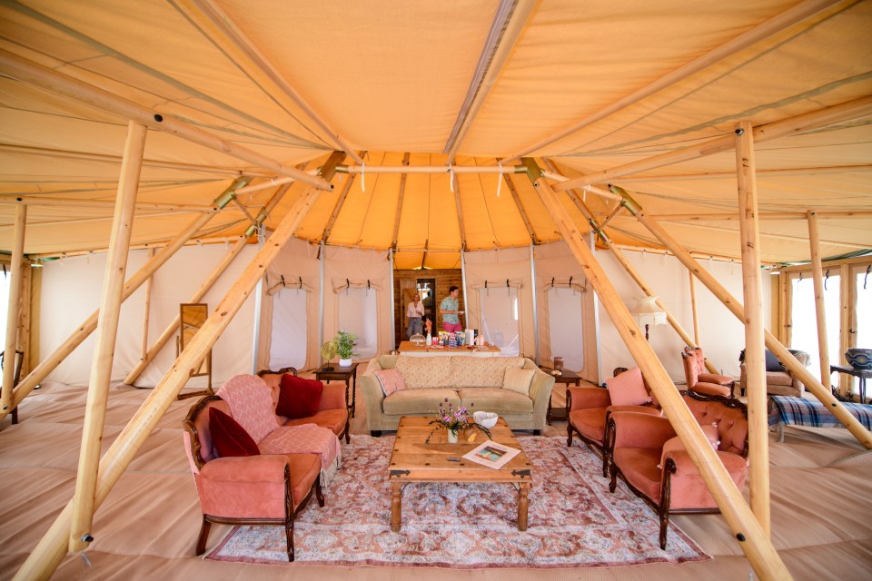 Interior of a large luxury tent with wooden poles, couches, and a rug.