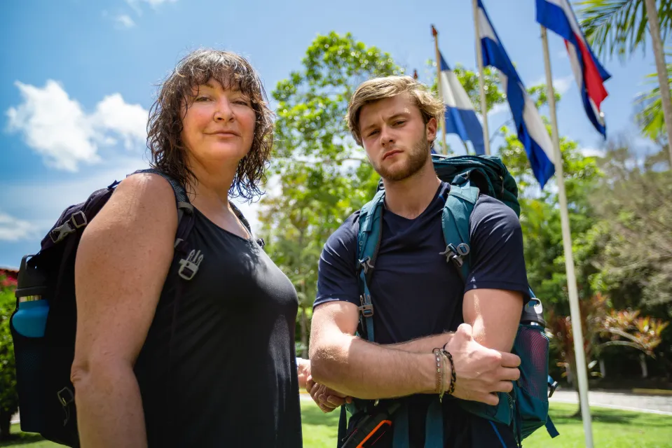 A woman and a young man with backpacks stand outdoors.