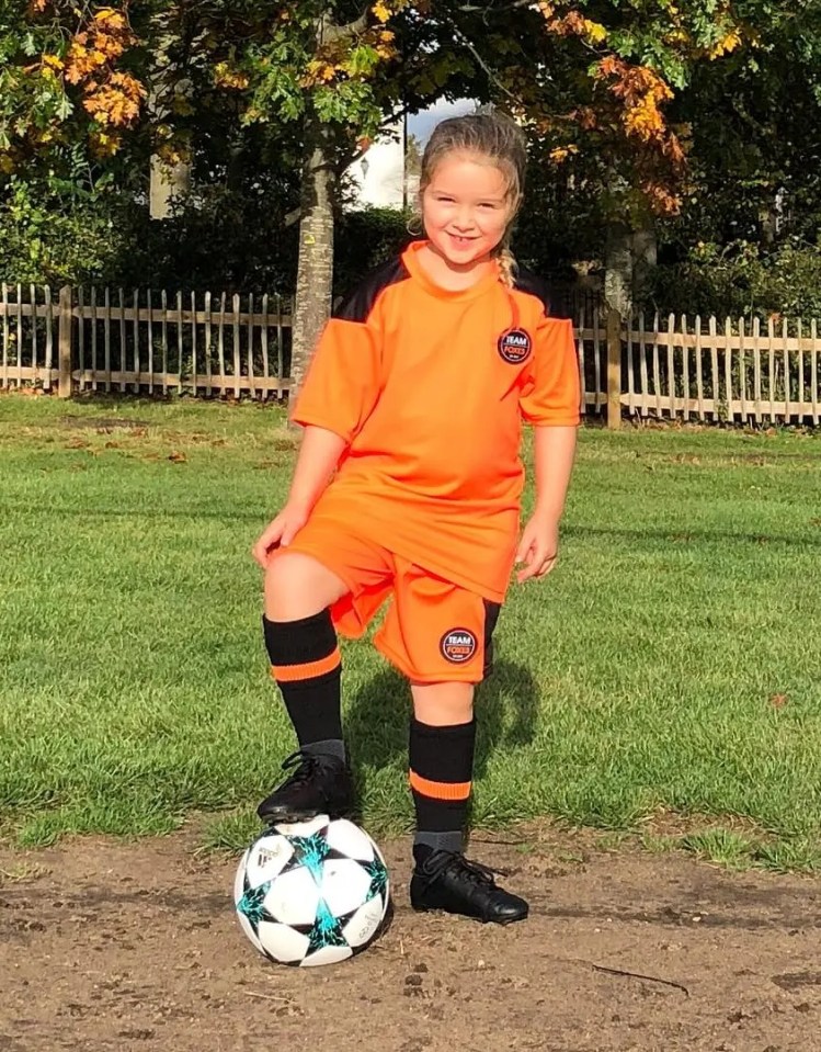 Girl in orange soccer uniform with soccer ball.