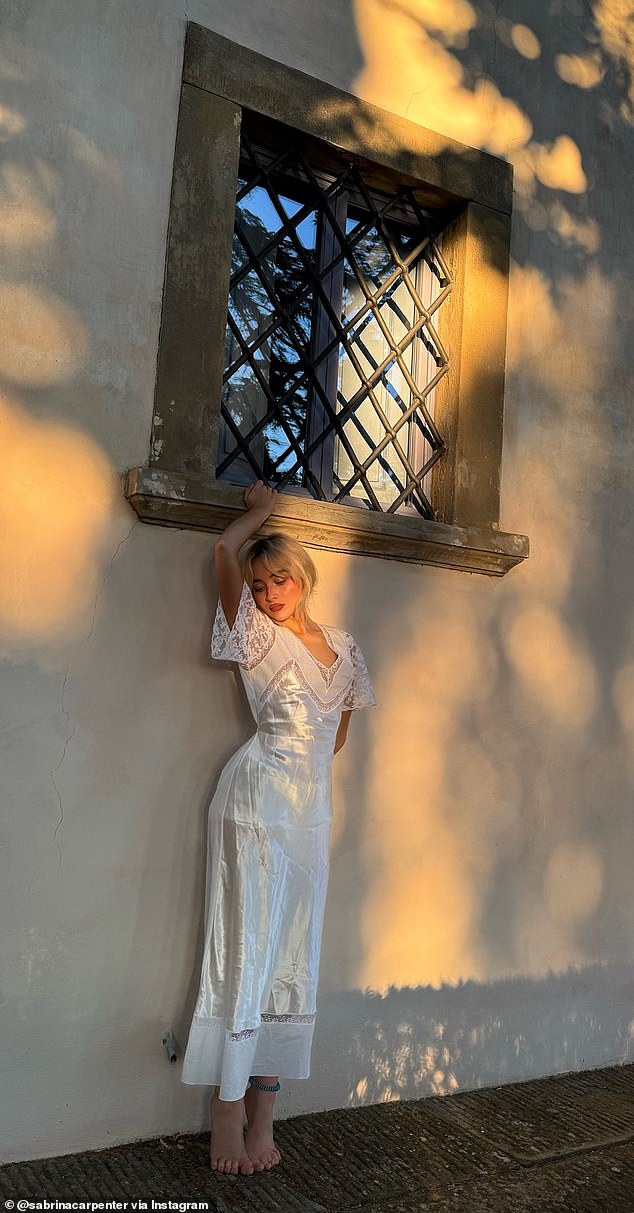 In another photo Carpenter looked line a muse wearing a cream satin and lace dress as she stood on her tiptoes beneath a wood framed window