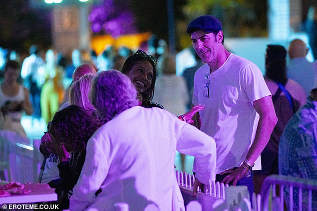 Sacha cut a casual figure in a white T-shirt and trousers as he smiled and chatted with another group