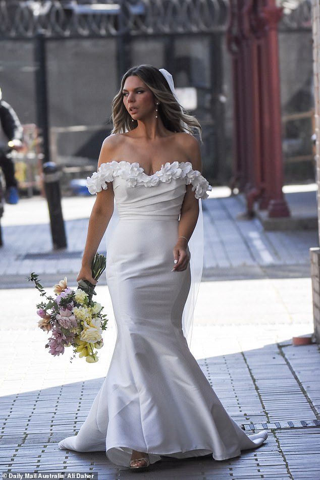 Clutching a vibrant bouquet of fresh blooms, she confidently made her way through the cobbled precinct as cameras rolled on her dramatic arrival, marking the official start of wedding week