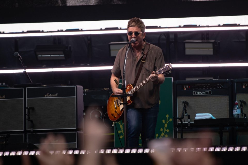 Liam Gallagher performing on stage with a guitar.