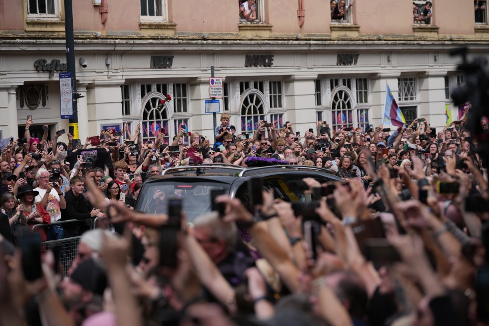 A large crowd of people using their phones to photograph a funeral procession.