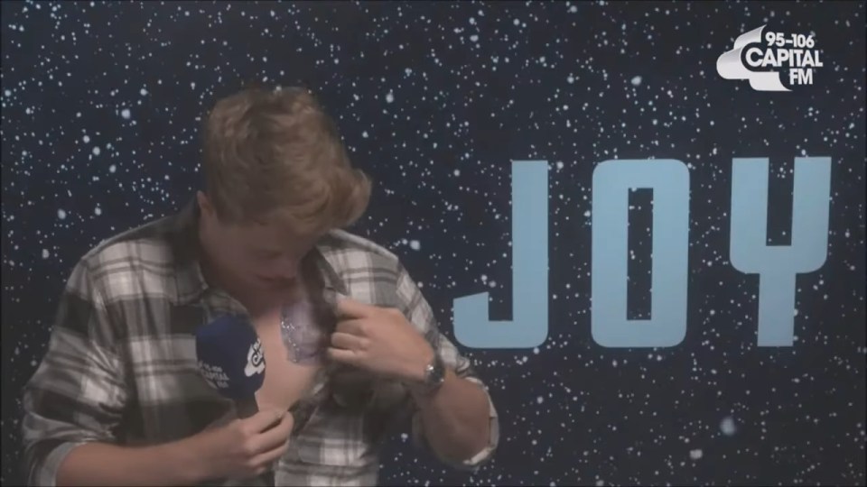 Man holding a microphone, looking down at a temporary tattoo on his chest.