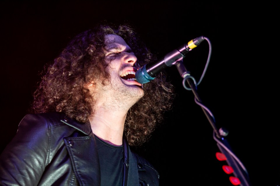 A man with curly hair singing into a microphone.