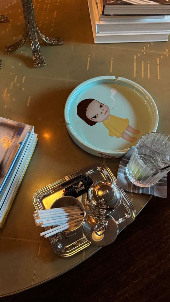 Ashtray with illustration of girl smoking, cocktail glass, and silver tray with cocktail stirrers.