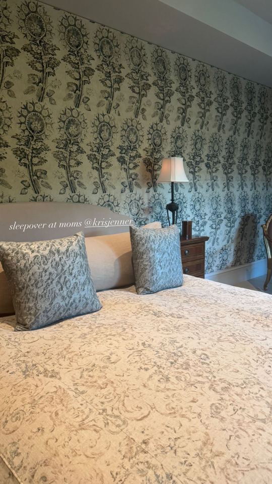 Bedroom with floral wallpaper and patterned bedding.