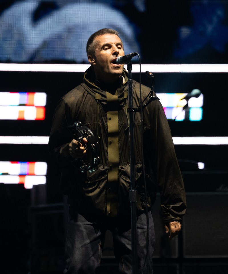 Liam Gallagher performing onstage with a tambourine.