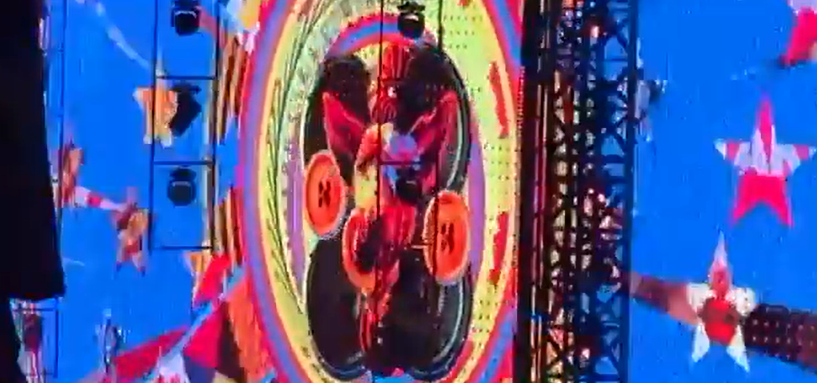 Screenshot of a concert stage with a large, colorful circular image and performers.