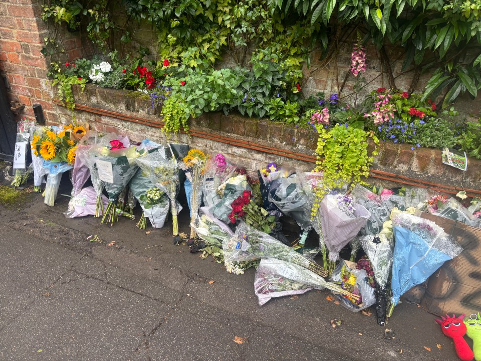 Floral tributes left on the ground outside a brick wall.